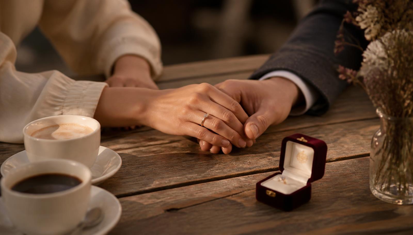 Hände eines Paares mit Verlobungsring und geöffneter Ringschatulle – KI-generiertes Symbolbild